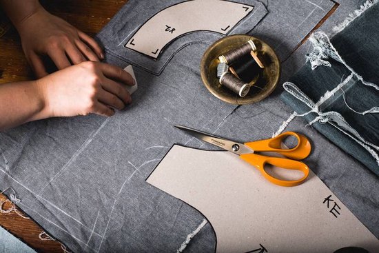 Fiskars schaar met oranje handgrepen ligt op een patroon op een stoffen ondergrond.