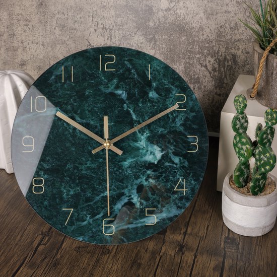 Groene marmerlook klok met gouden cijfers en wijzers, op een houten tafel naast planten.