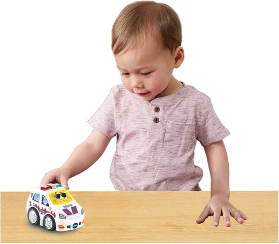 Een jongetje speelt met een wit politieauto speelgoed op een houten tafel.