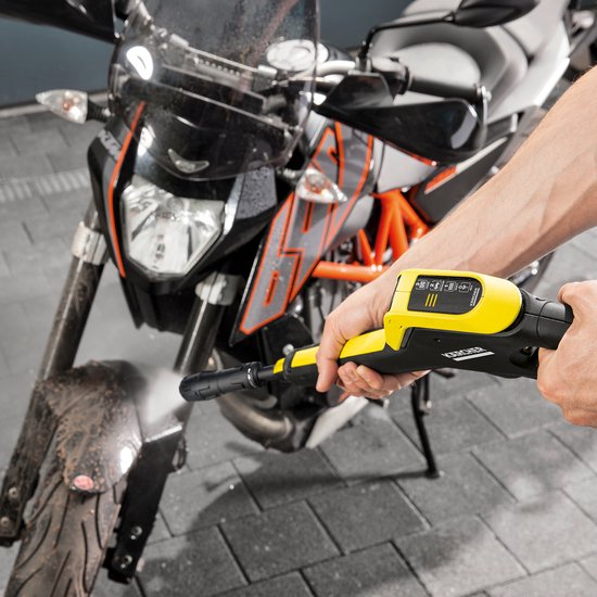 Een hand met een gele Kärcher hogedrukreiniger spuit een modderige motorfiets schoon.
