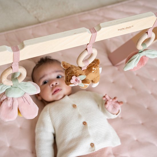 Baby ligt onder houten babygym met speeltjes: bloem, hertje en aardbei.