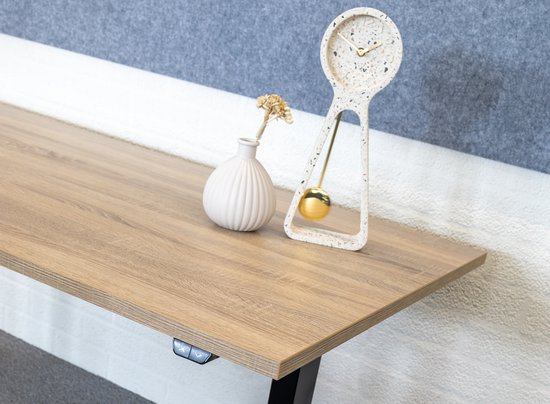 Een lichtbruin houten bureau met een decoratieve klok en vaasje, met een deel van een groene bureaustoel zichtbaar.
