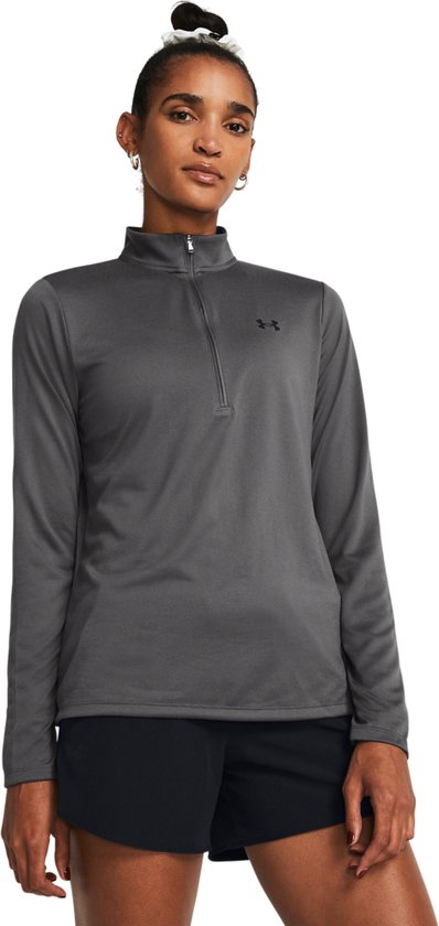 Model in grijze sporttrui met lange mouwen, ritskraag, zwart logo en zwarte short.