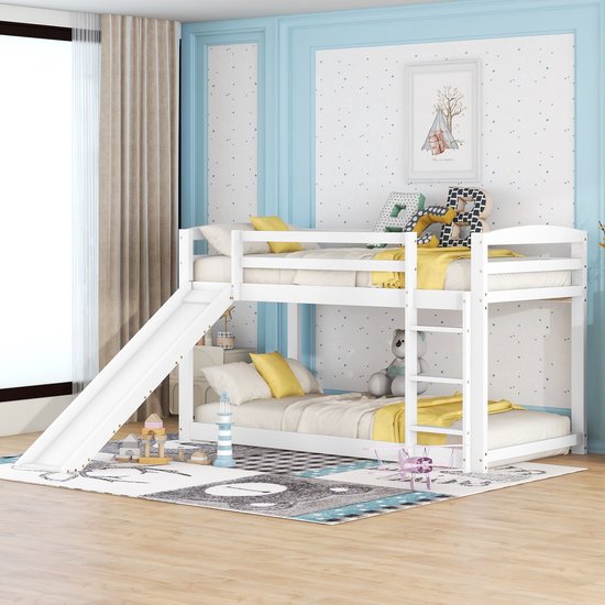 Wit stapelbed met ladder, glijbaan, gele dekens en kussens, in een kinderkamer.
