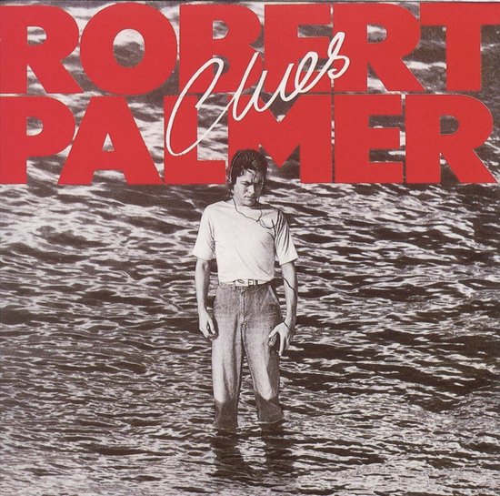 Robert Palmer staat in het water met een koptelefoon en een t-shirt met korte mouwen en een spijkerbroek.