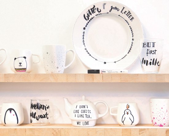 Mugs blancs décorés, un plat blanc à motif de flèche et l'inscription "better if you Letter", un verre avec "BUT first MILK", et une théière blanche avec du texte.