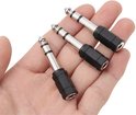 Drie 6.35mm naar 3.5mm audio adapters in een hand, met zilverkleurige aansluiting en zwart handvat.