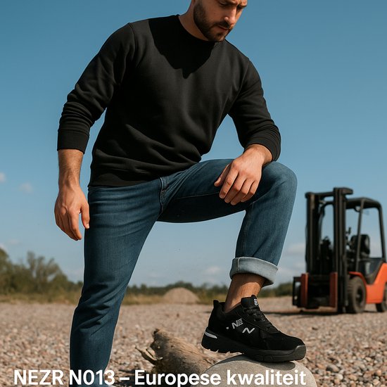 Man poseert met zwarte NezR N013 werkschoenen, jeans en een zwart sweatshirt, met heftruck op achtergrond.