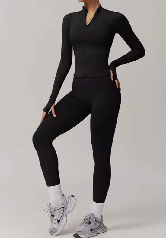 Model in een zwarte sportset: lange jas met rits en zwarte legging.