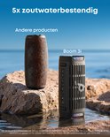 Zwarte Soundcore speaker naast een oudere luidspreker in ondiep water op rotsen, met tekst '5x zoutwaterbestendig'.
