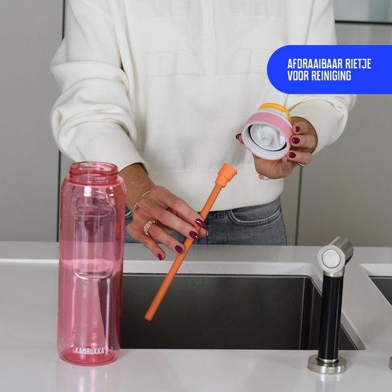 Une femme démonte une gourde Kambukka rose avec paille orange pour le nettoyage. La gourde fait 1L.
