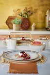 Een gedekte tafel met beige borden, mokken en kommen, geserveerd met pannenkoeken en fruit.