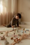 Jongen speelt zittend met een houten treinbaan, huisjes en figuren.