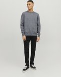 Man met een donkerblauwe gebreide trui met ronde hals en zwarte jeans.