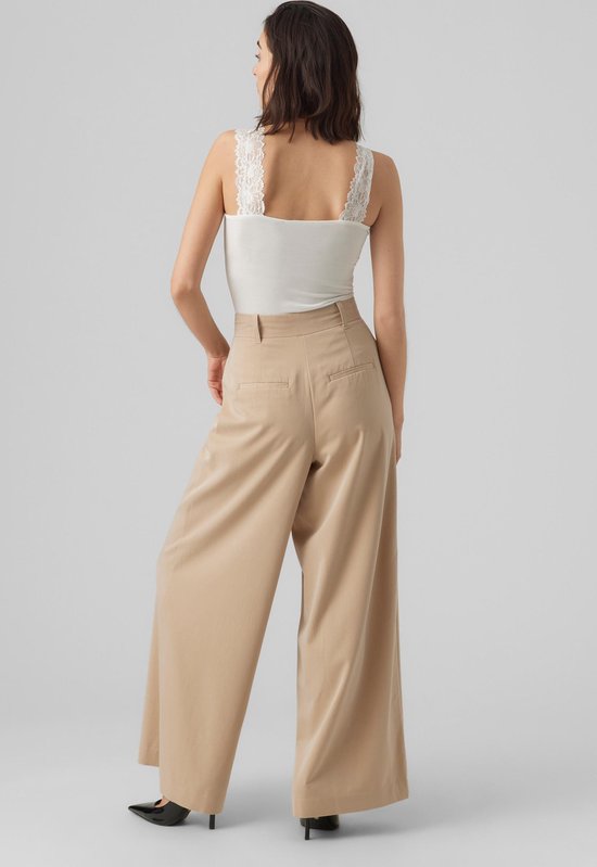 Achterkant model in wit kanten hemdje, beige wijde broek met hoge taille.