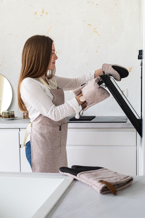 Een vrouw met een schort doet grijze pannenlappen aan om een ovenrek uit een oven te halen.
