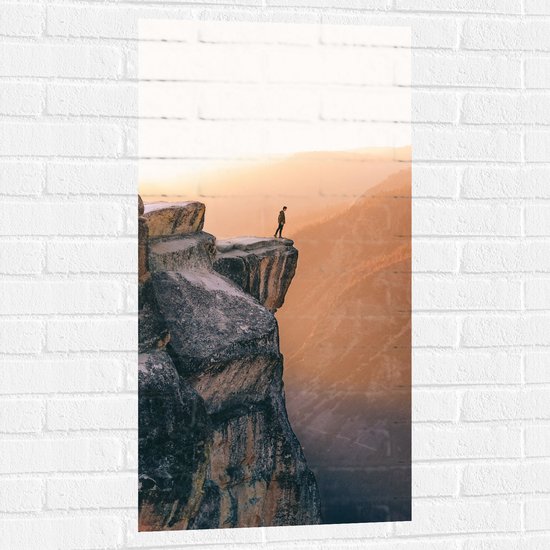 WallClassics - Muursticker - Man aan de Rand van Hoge Cliff met Zonlicht - 50x100 cm Foto op Muursticker