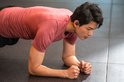 Un athlète masculin effectue un exercice de planche, portant des écouteurs noirs Shokz OpenFit Air.