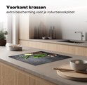 Zwarte inductiebeschermer met betonprint, bedekt met kruiden, knoflook, citroen en peperkorrels, op een aanrecht in een moderne keuken.