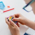 Un enfant tient un magnet Stitch diamond painting presque terminé. Le magnet montre Stitch sur fond jaune, partiellement recouvert de strass.