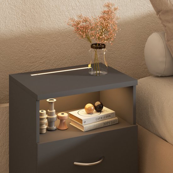 Donkergrijs nachtkastje met verlichting en decoratie: vaas met bloemen, boeken en decoratieve objecten.