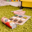 Houten koekjes op bakplaat, met rol koekjesdeeg, ovenwant en spatels op groen tapijt. Koekjes met witte icing, sprinkles, chocolade, groene en blauwe icing.