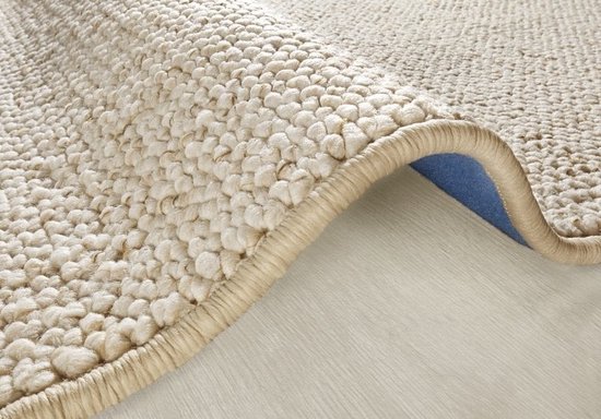 Detailopname van een crèmekleurig vloerkleed dat omhoog krult, met dikke, bobbelige lussen.