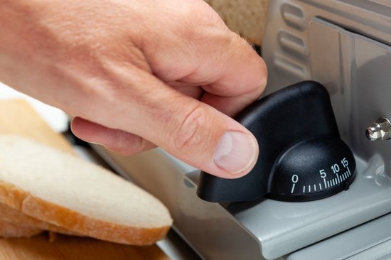 Hand draait een zwarte knop met instelbare diktemaat op een zilverkleurige snijmachine.