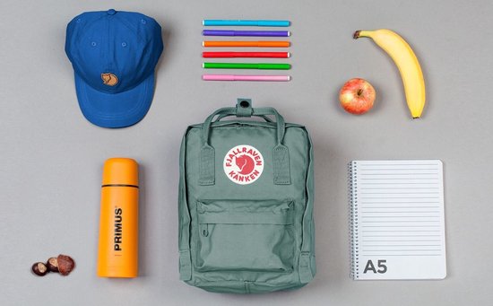 Groene Kånken Mini rugzak ligt met schoolspullen op een grijze achtergrond.