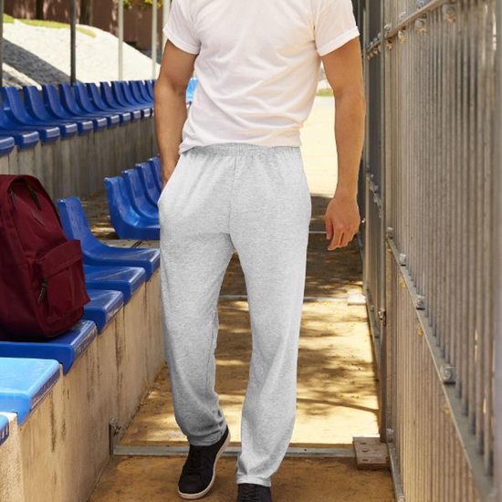Man in grijze joggingbroek en wit t-shirt, lopend bij een sportstadion.