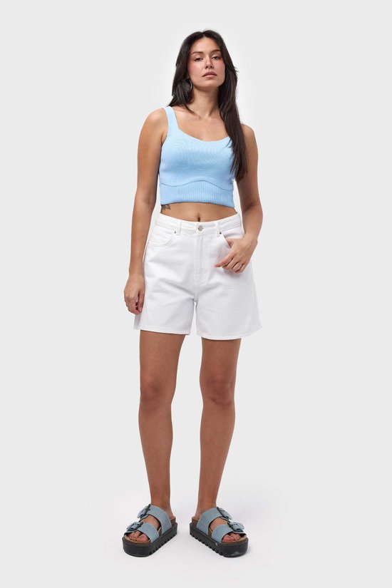 Model draagt een wit denim short en een blauwe crop top. Ze staat frontaal met een hand in de zak.