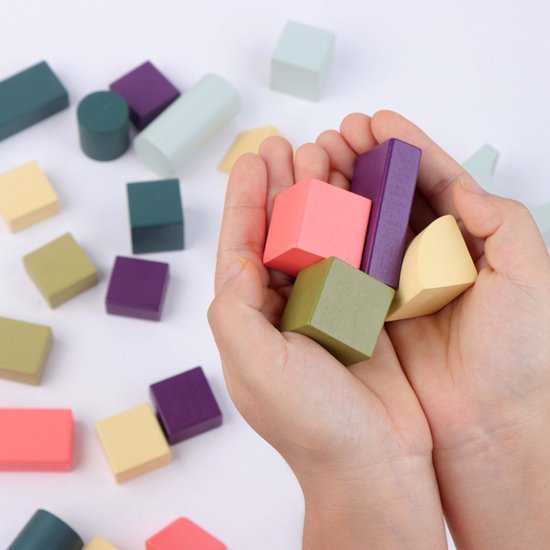 Kinderhanden houden houten bouwblokken vast: roze kubus, paarse staaf, groene kubus, gele wig.
