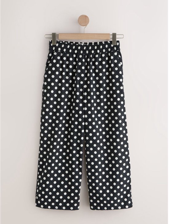 Een zwarte culotte met witte polkadotprint hangt aan een kledinghanger.