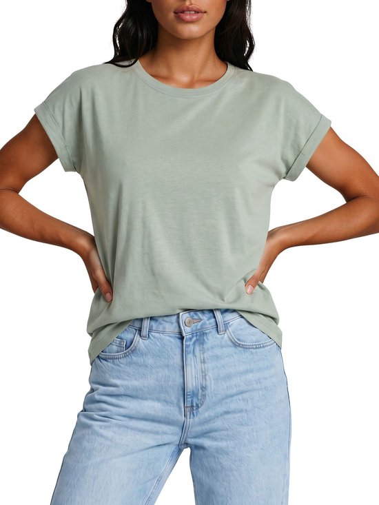 Model met lichtgroene effen top met opgerolde mouwen en jeans.