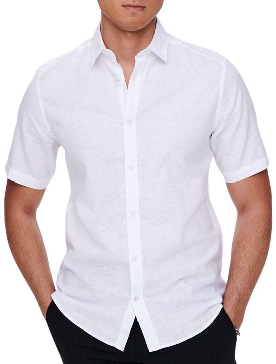 Witte linnenmix blouse met korte mouwen, gedragen door een man met zijn handen in de zakken van een zwarte broek.
