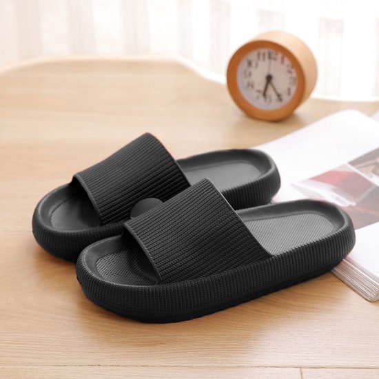 Paar zwarte, geribbelde EVA slippers op een tafel met een tijdschrift en wekker.