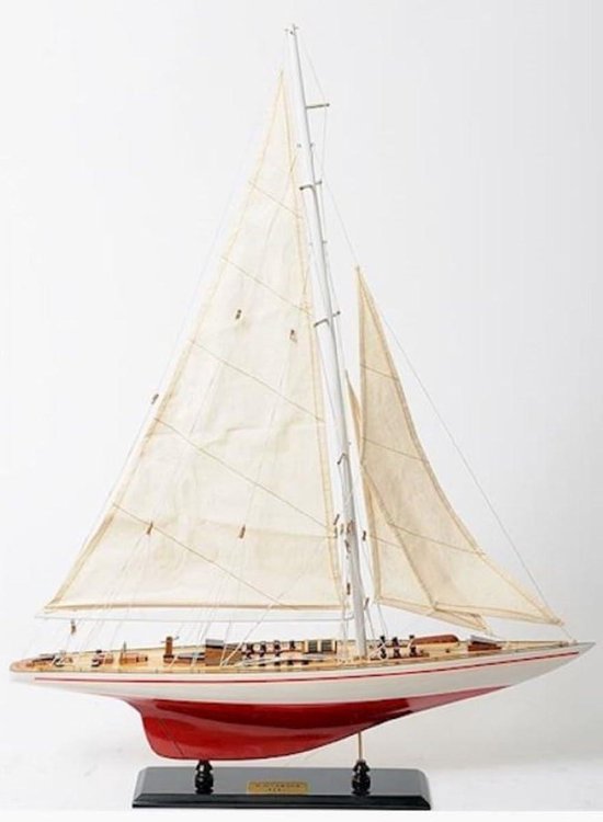 Houten zeilbootmodel met witte zeilen, rode romp en witte waterlijn, op een zwarte standaard.