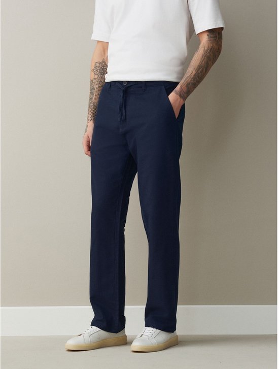 Man draagt donkerblauwe chino met rechte pijpen en een wit T-shirt.