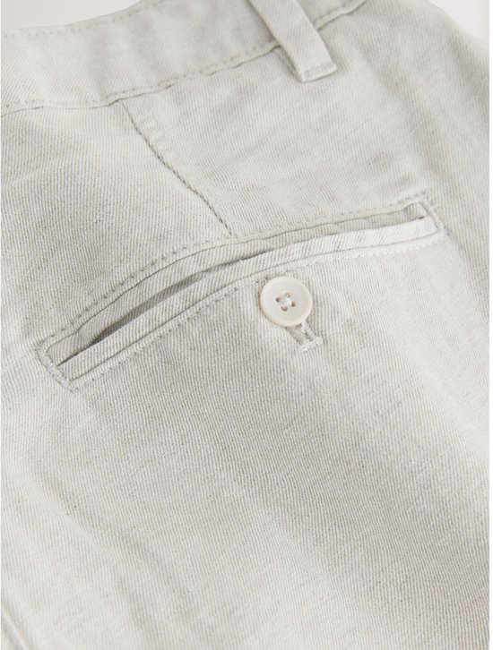 Detail van de achterzak van een lichtgrijze chino van katoen en linnen, met knoop.