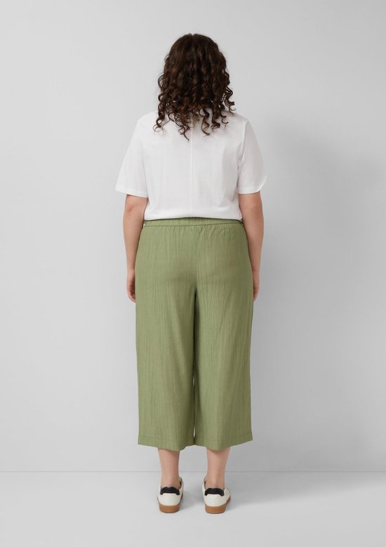 Vrouw, achterkant, draagt olijfgroene culotte met crinkle stof en witte sneakers.