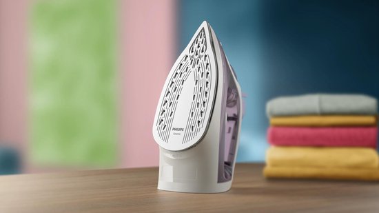 De witte en paarse zoolplaat van een Philips strijkijzer met vele gaatjes, naast een stapel kleding.