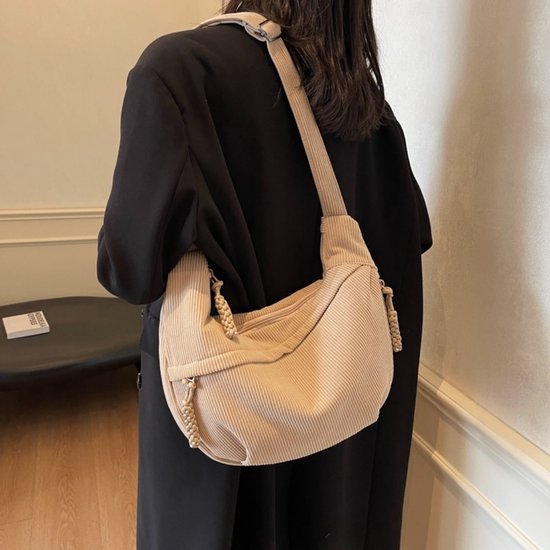 Lichtbruine corduroy crossbodytas gedragen door een model met zwarte jas, verstelbare schouderband.
