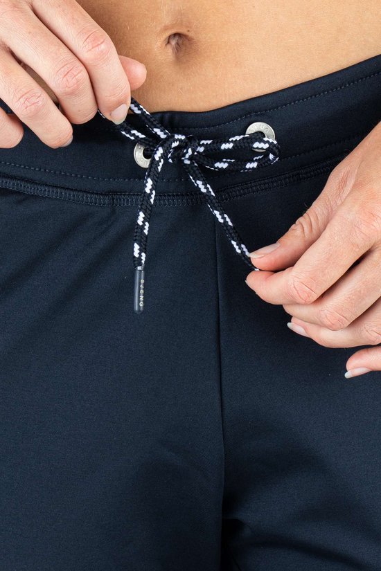Close-up van de tailleband van een donkerblauwe sportbroek, met handen die een trekkoord strikken.
