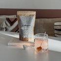 Bruine papieren zak met 'Collageen' etiket, een maatlepel met wit poeder en een glas roze drank.