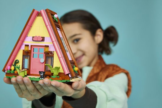 Kind houdt een Lego Friends speelgoedhuisje met roze accenten, een deur en katje vast.