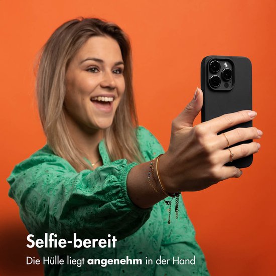 Een glimlachende vrouw met blond haar en een groene top neemt een selfie met een smartphone in een zwarte hoes. Tekst: Selfie-ready. De hoes ligt aangenaam in de hand.