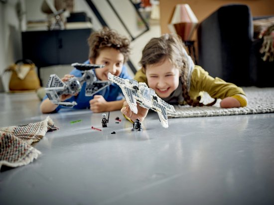 Twee kinderen spelen op de vloer met de LEGO Star Wars Mandalorian Fang Fighter en TIE Interceptor.