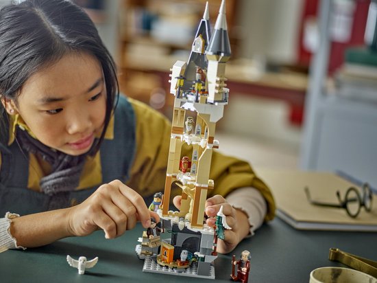 Une jeune fille construit une maquette LEGO de l'aile aux hiboux de Poudlard, avec des tourelles, des arches et des figurines de hiboux.