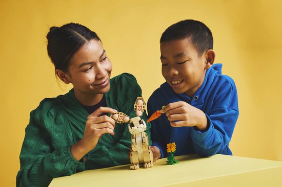 Femme et enfant construisent un lapin LEGO avec carotte et fleur.