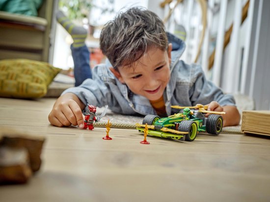 Een jongen ligt op de grond en speelt met de LEGO Ninjago racewagen (71828) en minifiguren.